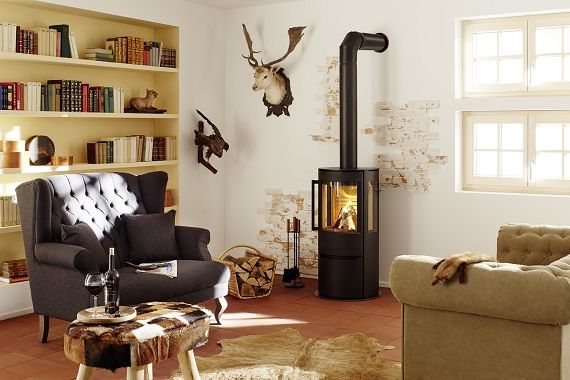 Gemütliches Wohnzimmer mit Kaminofen, Sessel, Bücherregal und rustikaler Dekoration.